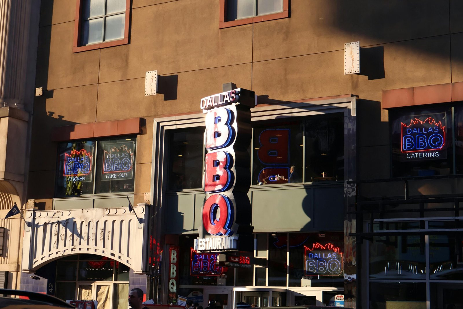Neon signage of Dallas BBQ Restaurant illuminated in an urban environment at sunset.